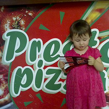 Criança de vestido rosa a ler a ementa à frente do letreiro da Presto Pizza